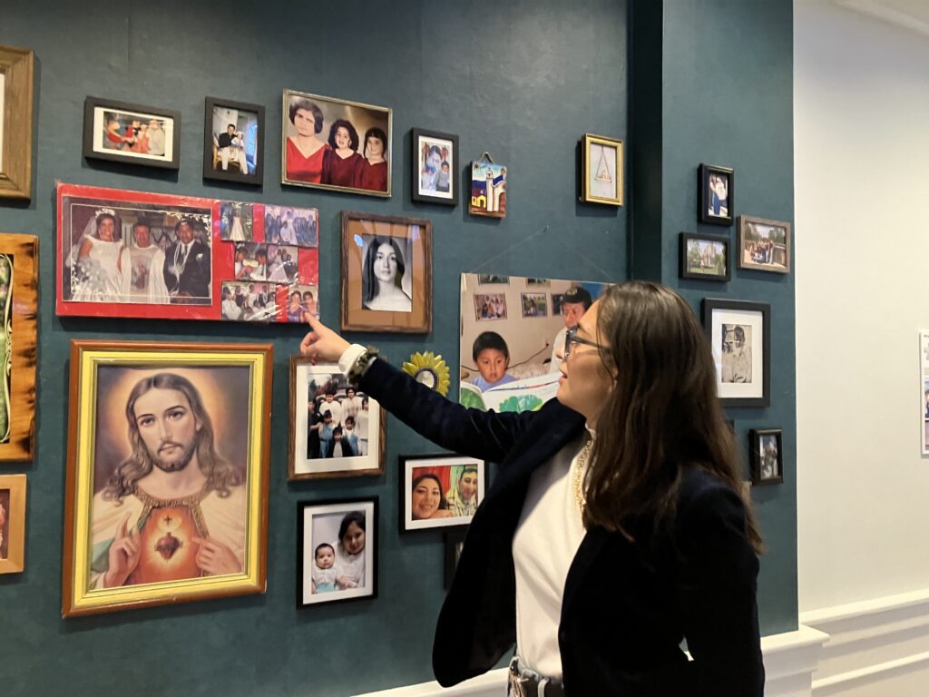 Photo of a woman pointing to a wall adorned with photographs.