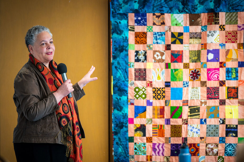 Photo of Susi Ryan gesturing toward a quilt.