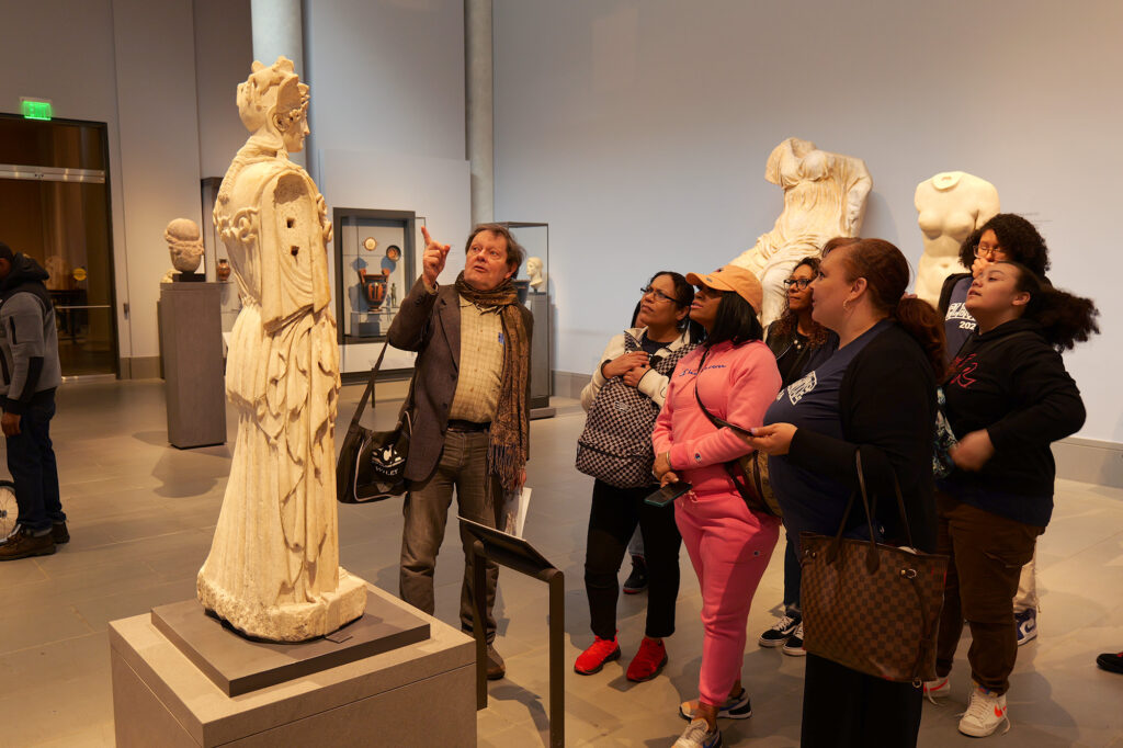 Students and a teacher look at a sculpture from classical antiquity.