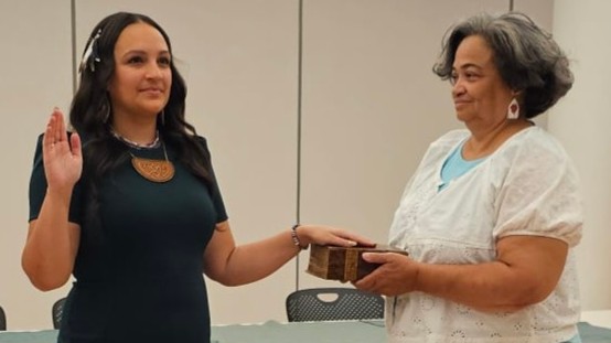 Brittney Walley (left) holds up her hand to take an oath on the Algonquian Bible. Cheryll Toney Holley, the Sonksq of the Hassanamisco Nipmuc Band, holds the book.